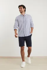 Camisa de lino a rayas verticales azules y blancas, de manga larga con puños abotonados y cuello clásico.