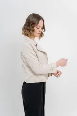 Chaqueta color beige de tela tipo gamuza con elastano, cuello solapa, manga larga con trabillas en hombro, bolsillos delanteros con cremallera metálica y cierre frontal con cremallera.