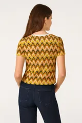 Top tejido de poliéster con estampado de zigzag en tonos amarillo, naranja, marrón y blanco. Tiene escote en V, mangas cortas y se anuda en el frente.