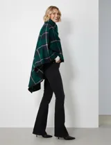 Capa corta de tejido grueso, color verde esmeralda con diseño de cuadros escoceses en azul marino y líneas finas en beige. Posee cuello alto que se cruza al frente y se cierra con un broche oscuro.
