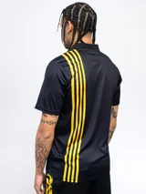 Remera polo de poliéster color negro con cuello clásico y tapeta de dos botones. Presenta el escudo del Club Atlético Peñarol bordado en el pecho y el año de fundación (1891) estampado en blanco. Tiene detalles en amarillo en los hombros y el escudo del club repetido en la parte inferior.