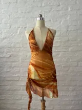 Vestido corto con estampado abstracto en tonos naranja, blanco y marrón. Diseño con escote halter y falda con volados.