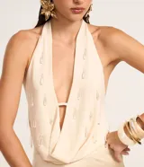 Blusa de crepé color crema, con escote drapeado y espalda descubierta. Presenta aplicaciones de piedras en el frente.