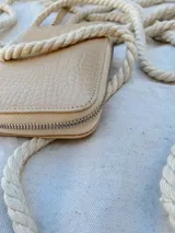 Billetera pequeña de cuero color beige con textura croco, forrada, con cierre metálico y pulsera de cuero.