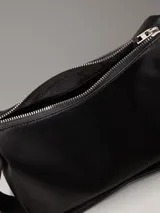 Bolso de hombro o cruzado de piel sintética negra, de forma rectangular y suave, con cierre superior de cremallera y correa ajustable con herrajes metálicos.