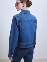 Chaqueta de jean celeste con cuello clásico, cierre frontal con botones metálicos y bolsillos de parche en el pecho.