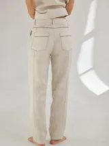 Pantalón largo color beige de lino, con bolsillos delanteros y traseros, cierre con botón y presillas para cinturón.