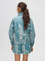 Campera rompevientos estilo biker con capucha desmontable, color celeste con estampado de nubes blancas y detalles en blanco.