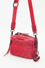 Bandolera negra de nylon matelassé con correa regulable, avíos metálicos, llavero de corazón y dijes desmontables.