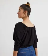Blusa de poliéster negra con mangas largas abullonadas, escote redondo con botones y bordado en el frente. Tiene volados en el ruedo y ajuste con lazos en los laterales.