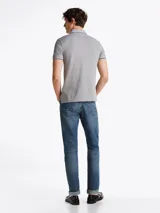 Chomba gris de algodón elástico con cuello y mangas ribeteadas en blanco y negro. Tiene cartera de tres botones, logo de Tommy Hilfiger bordado en el pecho y corte slim.