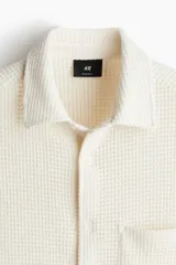 Camisa de manga larga en punto waffle color crema, con cuello inglés, tapeta lisa con botones y un bolsillo abierto en el pecho.