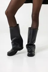 Bota de caña media color negro, de ecocuero, con base plana y corte holgado.