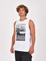 Musculosa blanca de cuello redondo y sisa amplia, con un estampado frontal de estilo fotográfico en blanco y negro que muestra un paisaje desértico y una construcción, acompañado por la palabra "wilderness" en color verde.