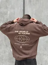 Canguro marrón con capucha ajustable con cordones, bolsillo tipo canguro y puños elásticos. Presenta un logo de un globo terráqueo y una flor bordados en el pecho.