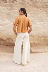 Blusa color camel con cuello mao, cierre frontal con botones y aberturas geométricas en hombros, mangas y cintura.