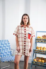 Vestido camisero corto con estampado a cuadros en tonos beige, rojo y azul. Tiene cuello camisero, botones frontales, bolsillo en el pecho y corte recto.