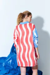 Túnica tipo vestido camisero corto con estampado de rayas onduladas verticales en colores rojo, blanco y azul. Tiene cuello camisero, cierre frontal con botones y mangas largas con puños abotonados.