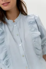 Blusa de lino color rojo con volados frontales que enmarcan el pecho, cuello redondo con mini volado y mangas 3/4 abullonadas con puño elástico. Presenta un cierre frontal con botones y una silueta relajada.