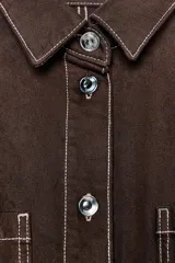 Mono corto color verde oliva, de denim con cuello solapa y manga corta. Tiene bolsillos delanteros y traseros, cintura elastizada en la espalda y cierre frontal con cremallera y botones metálicos.