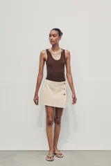 Falda pantalón corta color crudo, de tiro alto con delantero cruzado y cierre con cremallera oculta y botones.