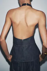 Top de cuello halter confeccionado en tejido denim azul. Detalle de pespuntes marcados a tono y espalda descubierta.
