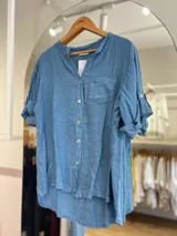 Camisa celeste de lino, con cuello mao, manga 3/4 con botón para sujetar, cierre frontal con botones y bolsillo de parche en el pecho.