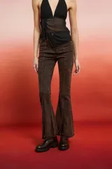 Pantalón de jean de tiro alto, color marrón oscuro con efecto lavado o desgastado, corte flare y tajo en el bajo. Presenta tachas doradas a lo largo de las costuras laterales.