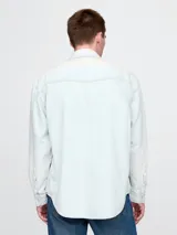 Camisa de jean celeste de manga larga con dos bolsillos frontales con solapa abotonada.