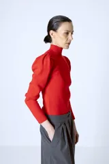 Polera roja de tejido de punto con cuello alto y mangas largas abullonadas en los hombros.