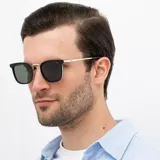 Lentes de sol INVU con montura cuadrada negra y dorada, lentes grises polarizadas y patillas plateadas.