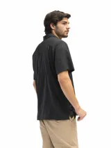 Camisa negra de manga corta con cuello clásico, cierre frontal con botones y bolsillo de parche en el pecho.