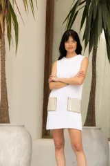 Vestido corto tejido en hilado de algodón en punto dolor, color blanco, con cuello redondo y sin mangas. Presenta dos bolsillos de lino aplicados en el frente.