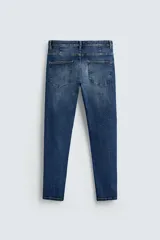 Pantalón de jean azul oscuro con efecto lavado y roturas en las rodillas, de corte ajustado al cuerpo desde la cintura hasta el tobillo.