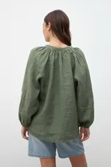 Camisa verde militar de crepe con escote en V, mangas largas abullonadas y detalle de cordón con borlas en el escote.