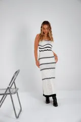 Vestido largo de punto calado blanco con rayas horizontales negras y breteles finos. El vestido tiene un corte recto y aberturas laterales en el ruedo. Las modelos llevan sombrero de estilo cowboy y botas de cuero.