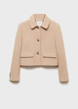 Chaqueta corta color beige de tweed con cuello camisero y cierre frontal con botones metálicos.