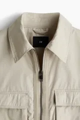 Campera color beige de corte holgado, con cuello camisero, cierre frontal y bolsillos superiores con solapa.