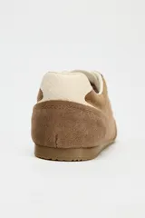 Zapatillas deportivas color marrón de piel con detalle de pespuntes, suela dentada, forro interior y parte trasera en contraste color crema. Cierre con cordones y acabado en punta redonda.