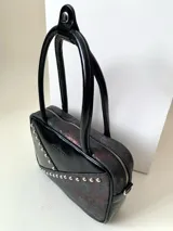 Cartera rígida negra de cuero con tachas plateadas y tres combinaciones de cuero diferentes que aportan textura. Tiene herrajes y cierre metálico plateado marca YKK. Cuenta con un asa fina para llevar al hombro o en la mano y una correa larga extra regulable.
