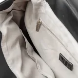Mochila negra de símil cuero con solapa y botones imantados. Tiene un bolsillo interno con cierre y dos abiertos, herrajes plateados, correa regulable y forro de algodón y poliéster.