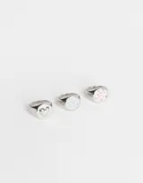 Set de tres anillos plateados con forma de sello. Uno presenta un corazón calado, otro una mariposa celeste y el tercero un moño rosa.