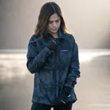 Campera cortaviento gris con estampado camuflado, cierre frontal completo, capucha ajustable y logo de la marca en el pecho.