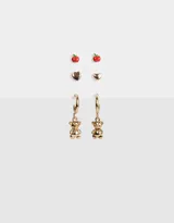 Set de tres pares de aros dorados: un par de aros tipo botón con forma de manzana roja, un par de aros tipo botón con forma de corazón y un par de aros colgantes con forma de oso.