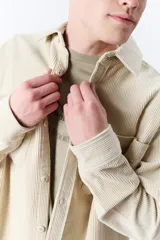 Sobrecamisa beige de pana con cuello clásico, cierre frontal con botones, mangas largas con puños abotonados y dos bolsillos de parche en el pecho.