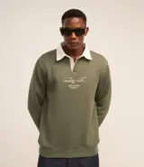 Buzo verde militar de algodón y poliéster con cuello polo blanco, mangas largas y puños ajustados. Presenta un bordado con lettering en el frente.