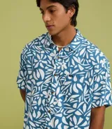 Camisa de manga corta para hombre, confeccionada en viscosa con un calce relajado. Presenta un diseño con estampa floral en blanco sobre fondo azul, cuello con solapa, cierre frontal de botones y un bolsillo en el pecho.
