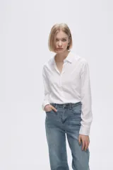Camisa blanca de manga larga con cuello clásico y cierre frontal con botones. Corte recto y holgado.
