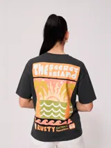 Remera negra de algodón con corte holgado y estampado frontal con el texto "Rusty Australia Mermaid Beach" en colores naranja, verde y amarillo.