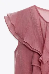 Top color rosado de tela semitransparente, con cuello redondo, sin mangas y volantes en el frente. Cierre con abertura y botón en la espalda.